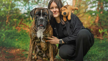 gemeinsames Fotoshooting mit Hund Boxer Baxter mit seiner Besitzerin Kopf an Kopf in der Hocke im Wald mit seinem Lieblingskuscheltier auf der Schulter